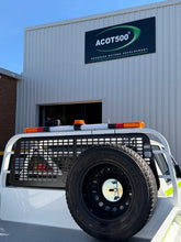 Back of a vehicle with a tire and guard, parked in front of a building with an ACOT500 sign.